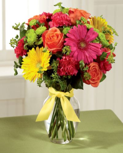 <p>Celebrating life with colorful blooms that inspire and delight, this flower bouquet is ready to create a happy moment for your recipient that they will never forget. Orange roses, hot pink gerbera daisies, yellow gerbera daisies, hot pink carnations, green button poms, bupleurum, and lush greens mingle together to create a sunlit display while seated in a classic clear glass vase tied at the neck with a yellow satin ribbon for a sweet effect.</p>
