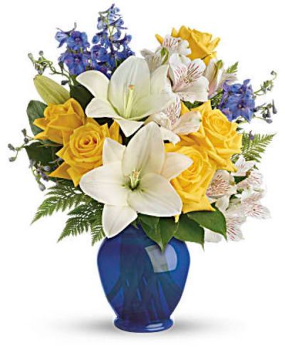 <p>Like a sunny day at the shore, this bright bouquet invigorates and inspires! Radiant yellow roses, white lilies and blue delphinium are expertly arranged in our bold blue plastic ginger jar.<br />
Sunny yellow roses, white asiatic lilies, white alstroemeria, and blue delphinium are arranged with leatherleaf fern and lemon leaf.</p>