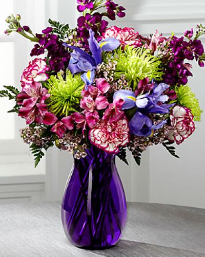 <p>Blooming with rich color and undeniable texture, this stunning bouquet expresses love and gratitude with each perfect flower. Blue Iris, fragrant purple gilly flower, purple Peruvian Lilies, purple bi-color carnations, green spider chrysanthemums, clusters of pink wax flower, and lush greens create a fascinating display presented in a deep purple glass vase with modern lines to create a sophisticated look.</p>